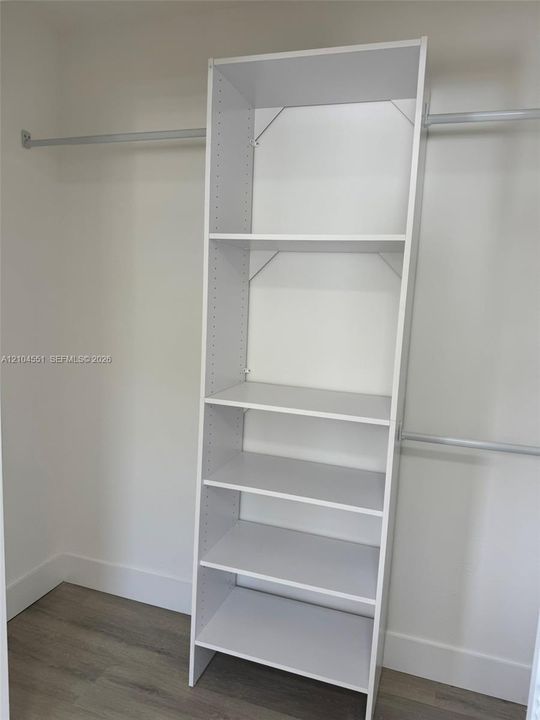 Custom walk-in closet featuring white built-in shelving, adjustable storage tiers, and dual metal hanging rods over wood-finish flooring