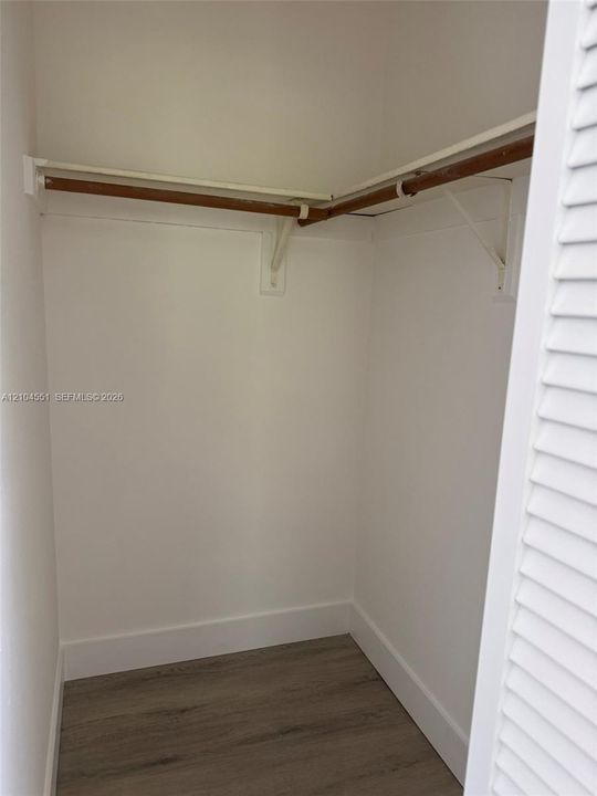 Storage area featuring wood-finish flooring, white louvered doors, and built-in shelving with a hanging rod