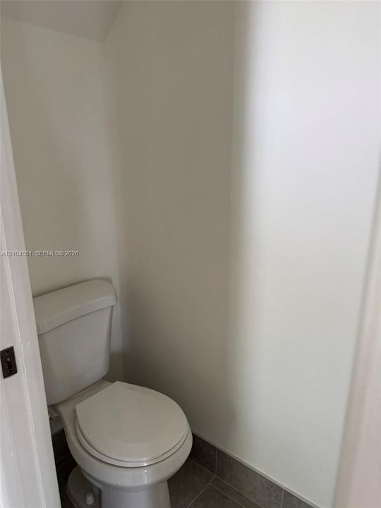 Enclosed space featuring a white porcelain toilet and neutral-toned tile flooring