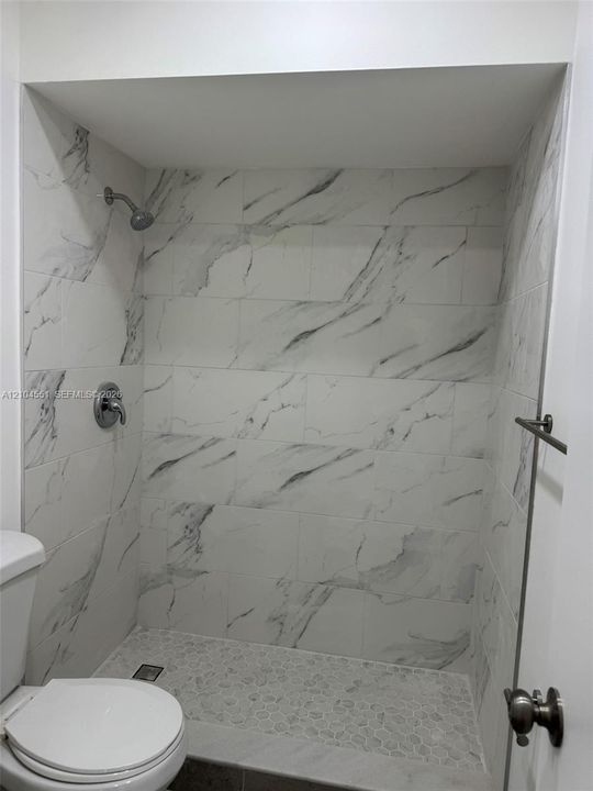 Walk-in shower featuring large-format stone-patterned wall tile, pebble-stone flooring, and chrome fixtures