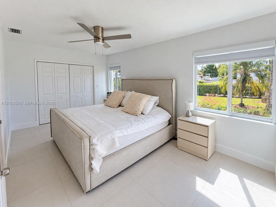 Neutral-toned ceramic tile flooring, dual-panel closet doors, ceiling fan with integrated lighting, and large windows providing natural illumination