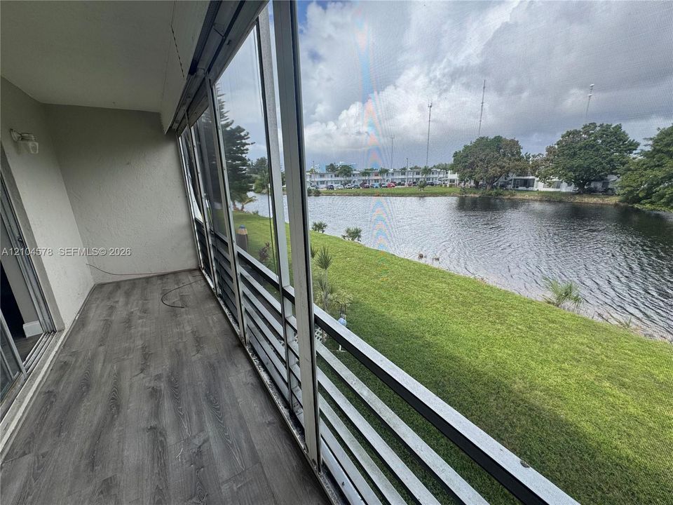 Screened-in balcony featuring wood-finish flooring, metal railing, and direct water frontage