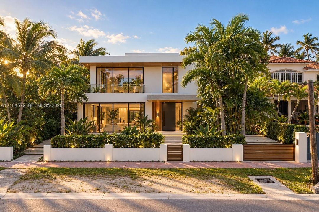 Contemporary architecture with expansive glass panels, a flat roof, a private balcony, a modern entry door, and a manicured tropical landscape