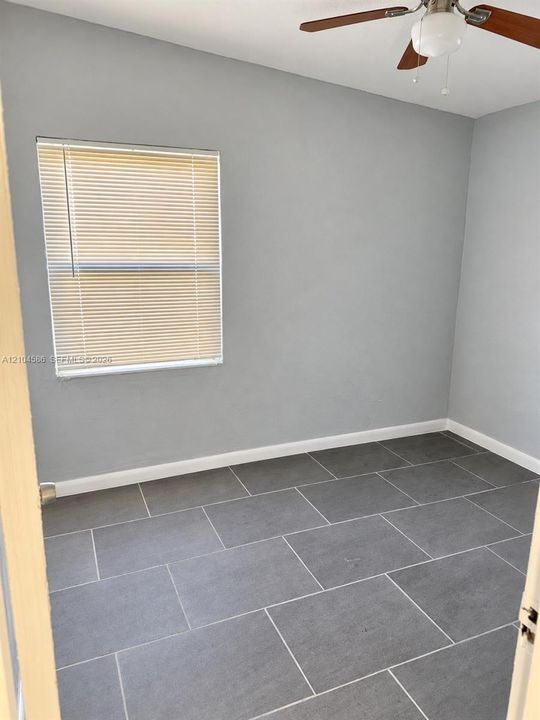 Neutral-toned interior room featuring large-format tile flooring, a window with horizontal blinds, and a ceiling fan with integrated light fixture