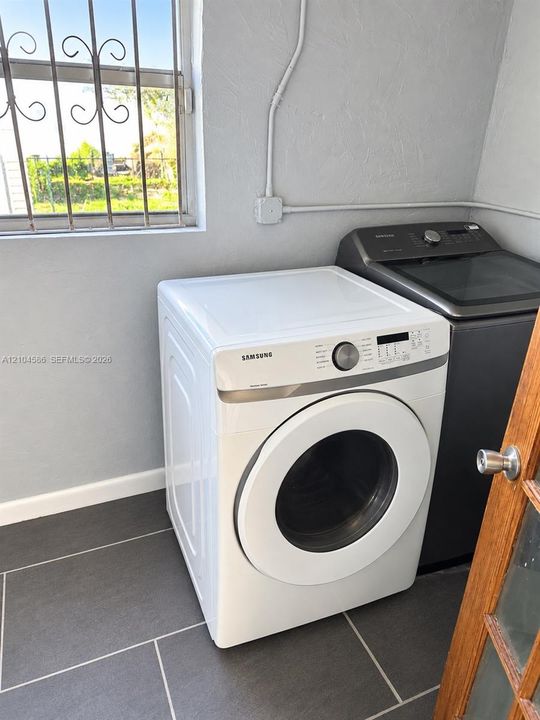 Laundry space featuring large-format grey tile flooring, window with protective security bars, and surface-mounted conduit