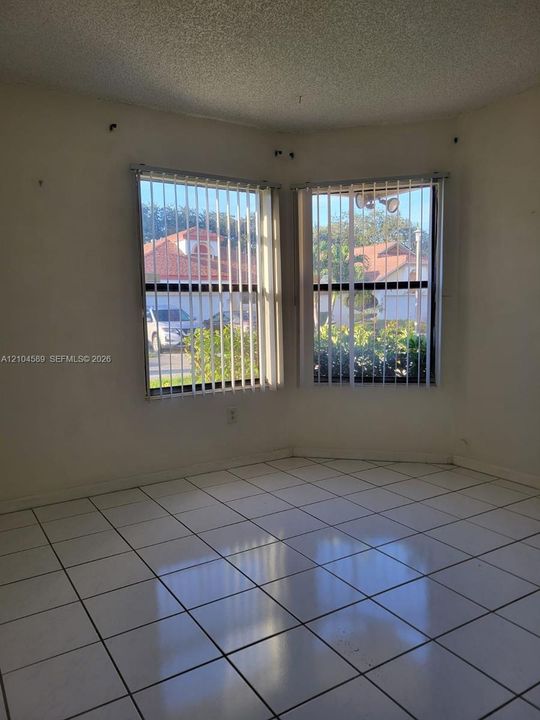 Corner room featuring white ceramic tile flooring and large windows with vertical blinds
