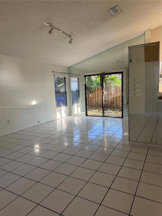Vaulted ceiling with textured finish, large format ceramic tile flooring, and sliding glass door with vertical blinds