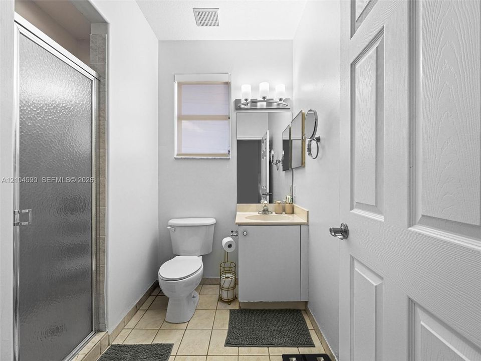 Bathroom featuring a shower stall with a textured glass door, single-basin vanity with a solid surface countertop, rectangular mirror, three-light fixture, and tiled flooring