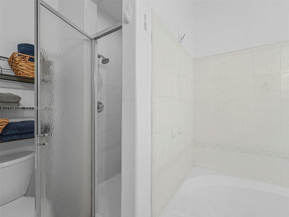 Shower stall with a textured glass door, chrome shower head, and large-format tile surround, accompanied by an integrated soaking tub featuring decorative tile detailing