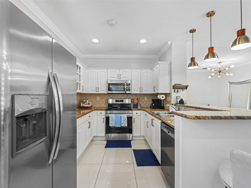 Kitchen featuring white shaker-style cabinetry, stone-finish countertops, stainless steel appliances, tile flooring, and pendant lighting