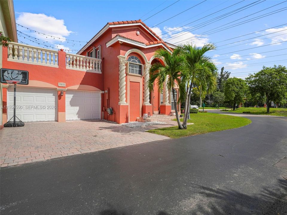Exterior featuring a stucco facade, arched entryway with spiral columns, balcony with stone-style balustrade, two-car garage, and a paver driveway