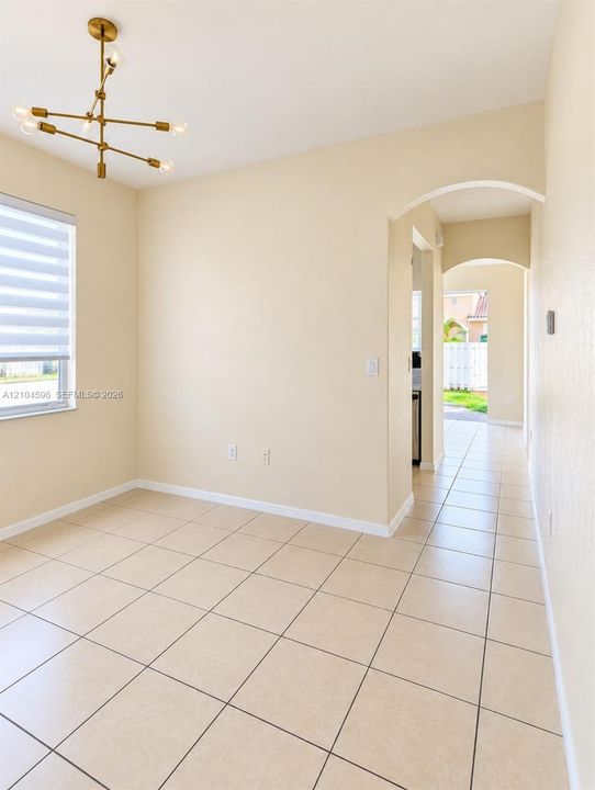 Interior space featuring large-format tile flooring, a modern multi-arm brass finish chandelier, neutral wall tones, and architectural arched doorways