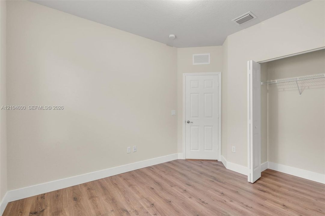 Interior room featuring neutral-toned walls, wood-finish flooring, a solid-core interior door, and a walk-in closet with built-in wire shelving