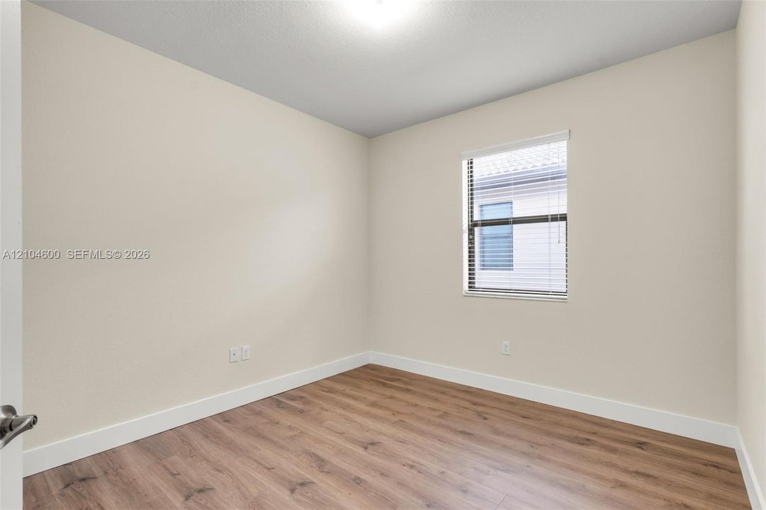 Neutral-toned interior space featuring wood-finish flooring and a single-pane window with horizontal blinds