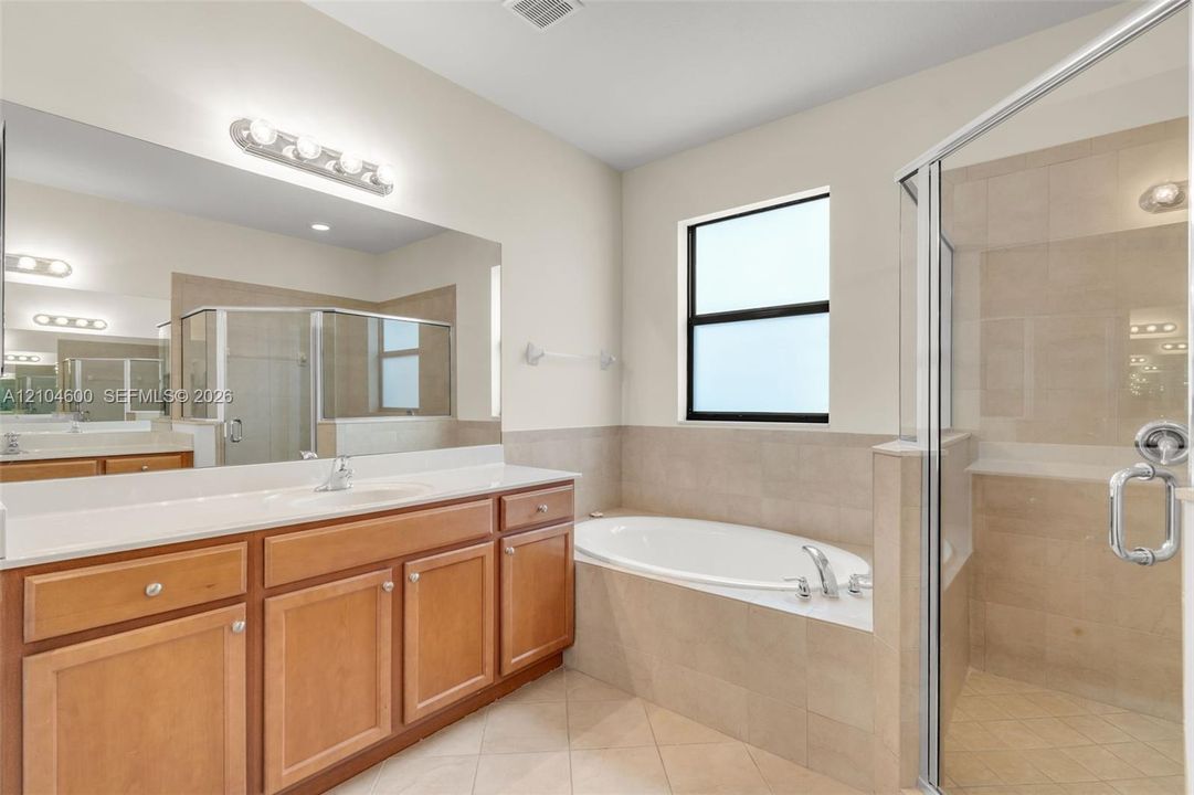 Bathroom featuring a large vanity with stone-surfaced countertop, drop-in sink, oversized wall-to-wall mirror, separate soaking tub, and a glass-enclosed shower with tile surround
