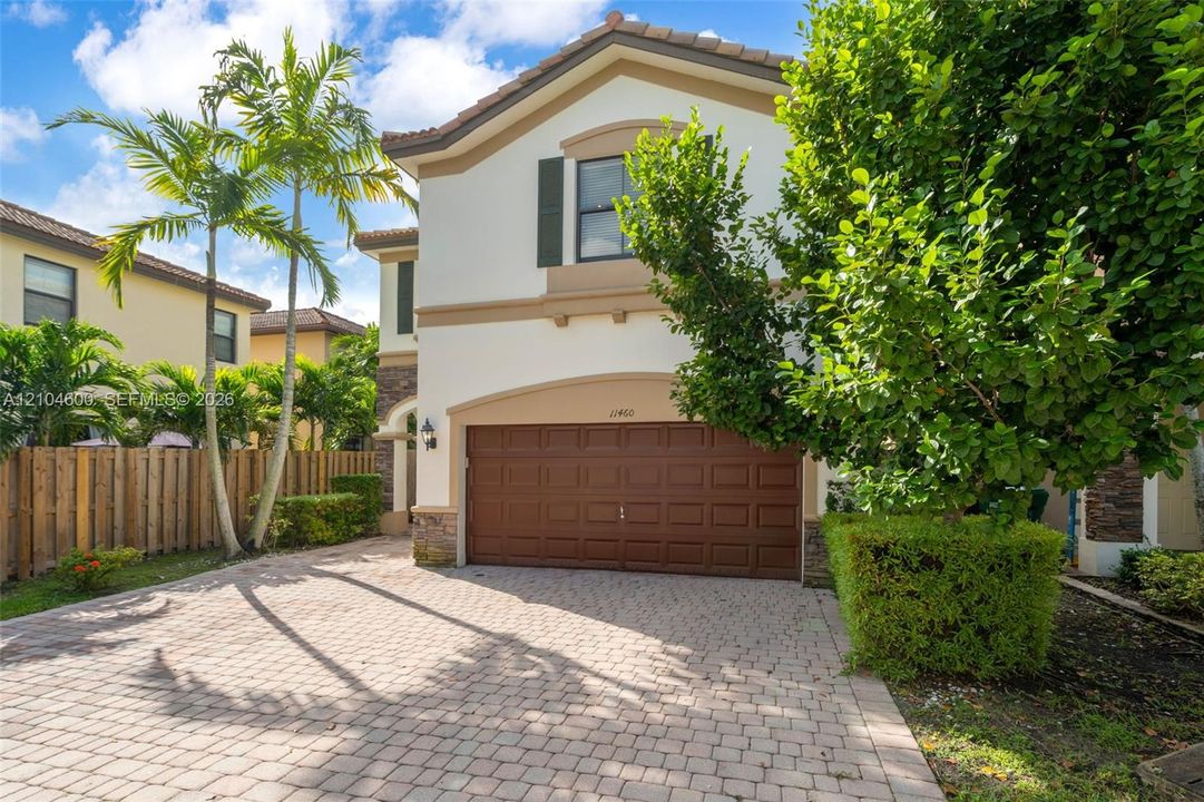 Two-story stucco exterior featuring stone veneer accents, a tiled roof, an attached two-car garage, and a paved stone driveway