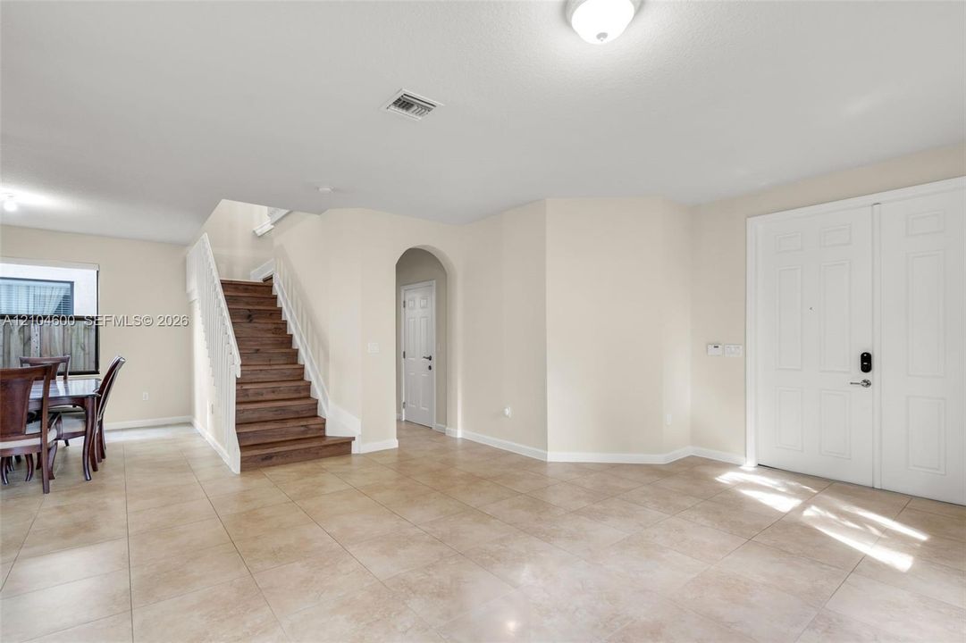 Open interior featuring large-format ceramic tile flooring, a staircase with wood-finish treads and white balusters, a double-door entryway, and an arched doorway