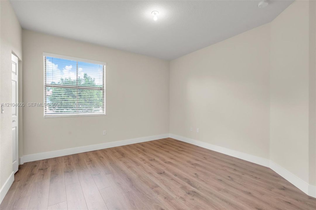 Neutral interior space featuring wood-finish flooring, light-toned walls, and a window with horizontal blinds