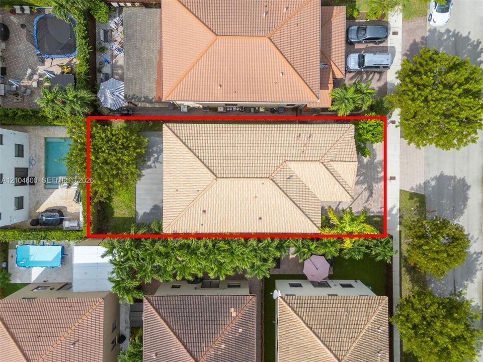 Aerial view of property featuring a hip roof design, concrete tile roofing, paved driveway, and established perimeter landscaping