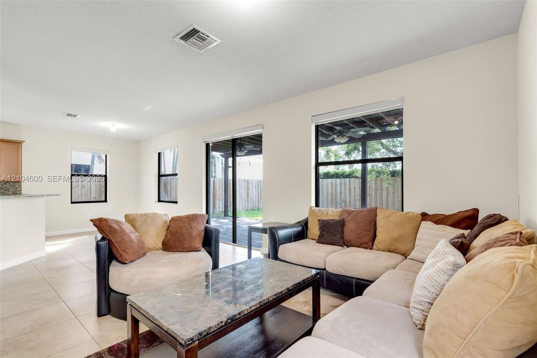 Open-concept interior featuring large-format tile flooring, oversized windows with window treatments, and sliding glass doors with direct access to a covered patio