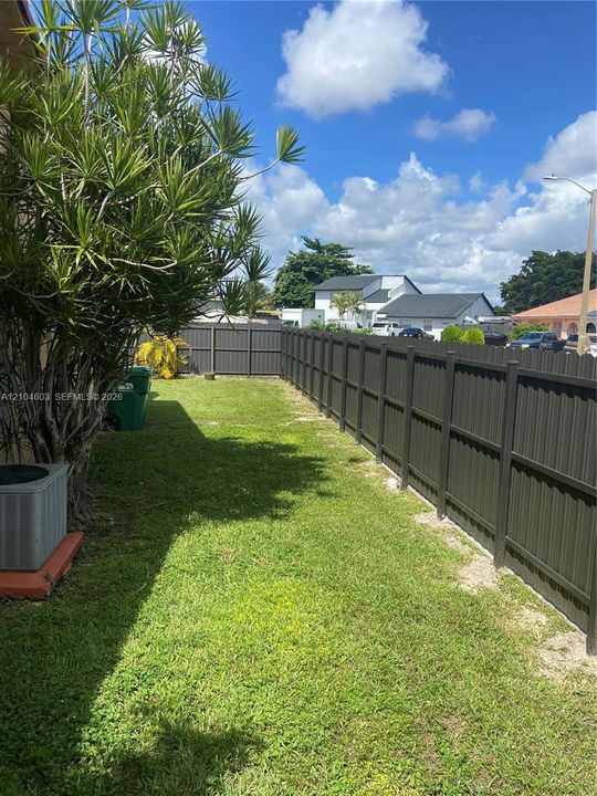 Fully fenced backyard featuring a grassy expanse and mature landscaping