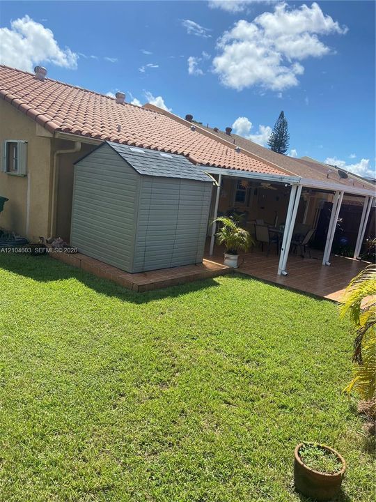 Expansive green lawn, covered patio, terra cotta tile roof, and exterior storage shed