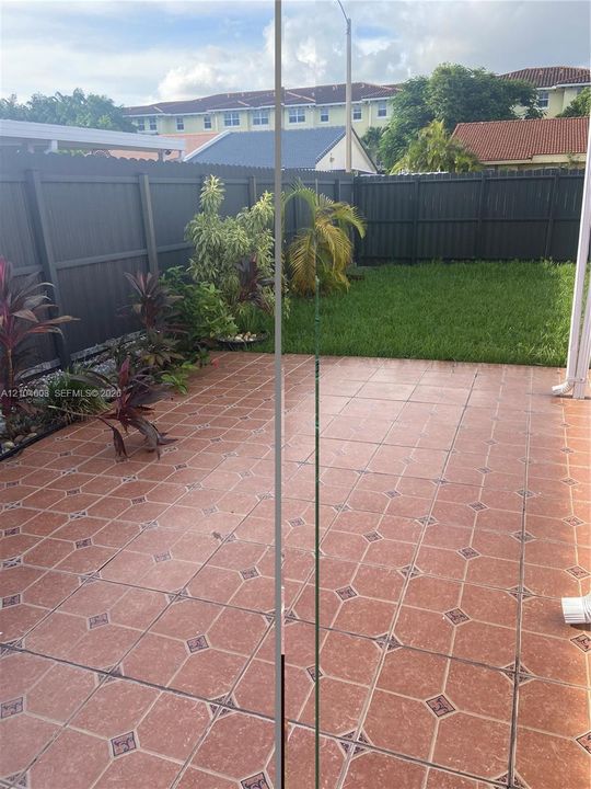 Tiled patio area with a privacy fence, lush planting beds, and a grassy yard