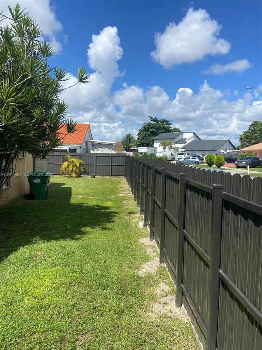 Expansive backyard featuring a manicured lawn, established landscaping, and a dark privacy fence