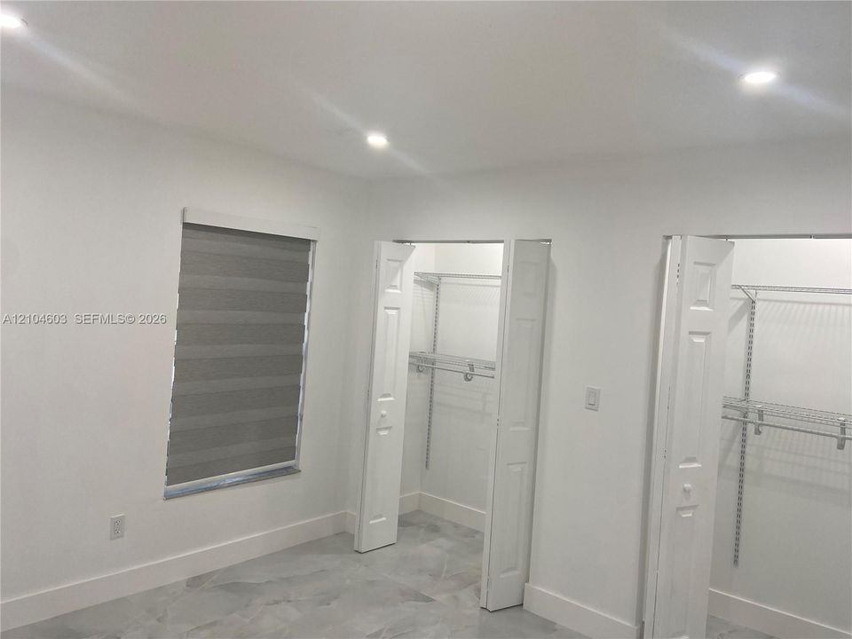 Recessed lighting illuminates the space, featuring a window with layered shades and large bi-fold closet doors