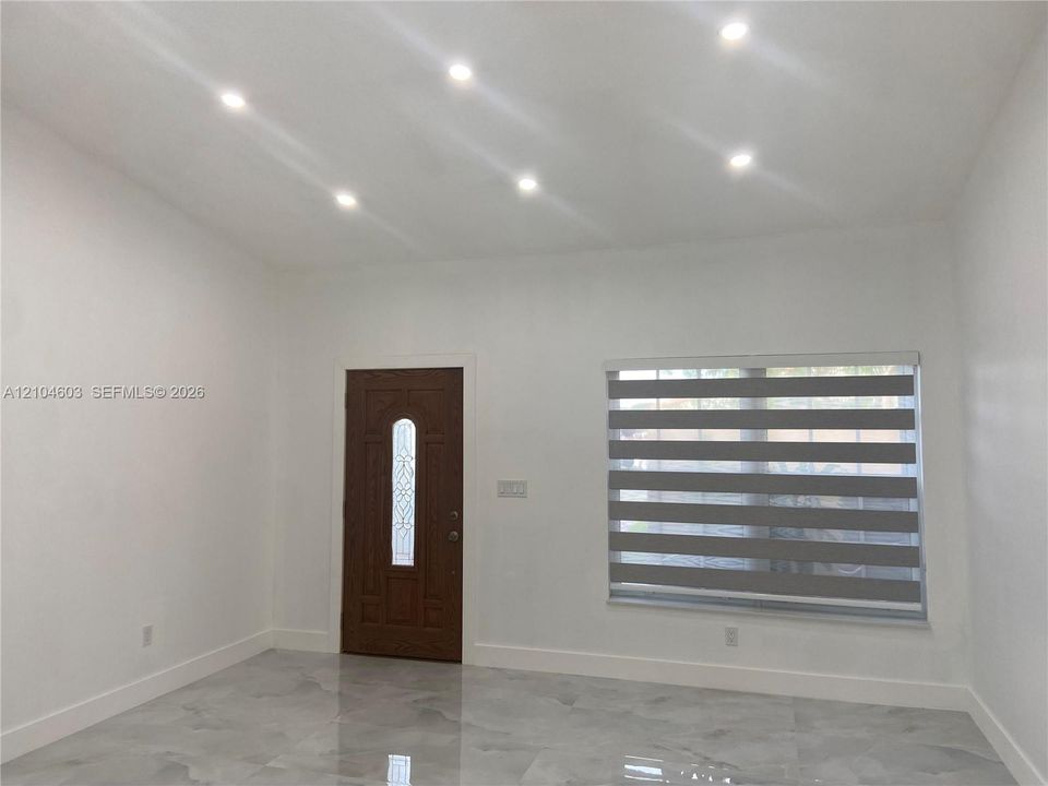 Recessed ceiling lighting, patterned window blinds, decorative entry door with glass insert, and polished tile flooring