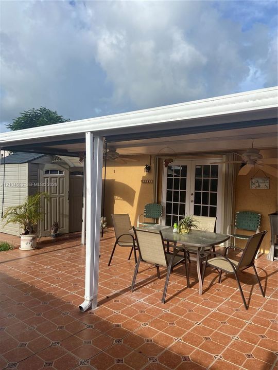 Covered patio with patterned tile flooring, exterior french doors, and a storage shed