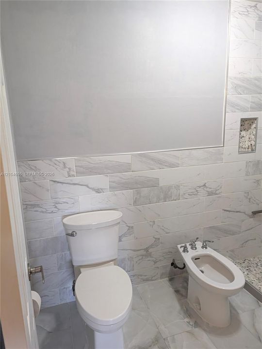 Wall-mounted mirror, large-format tile flooring, horizontal stone-pattern wall tiling, integrated wall niche, and porcelain plumbing fixtures