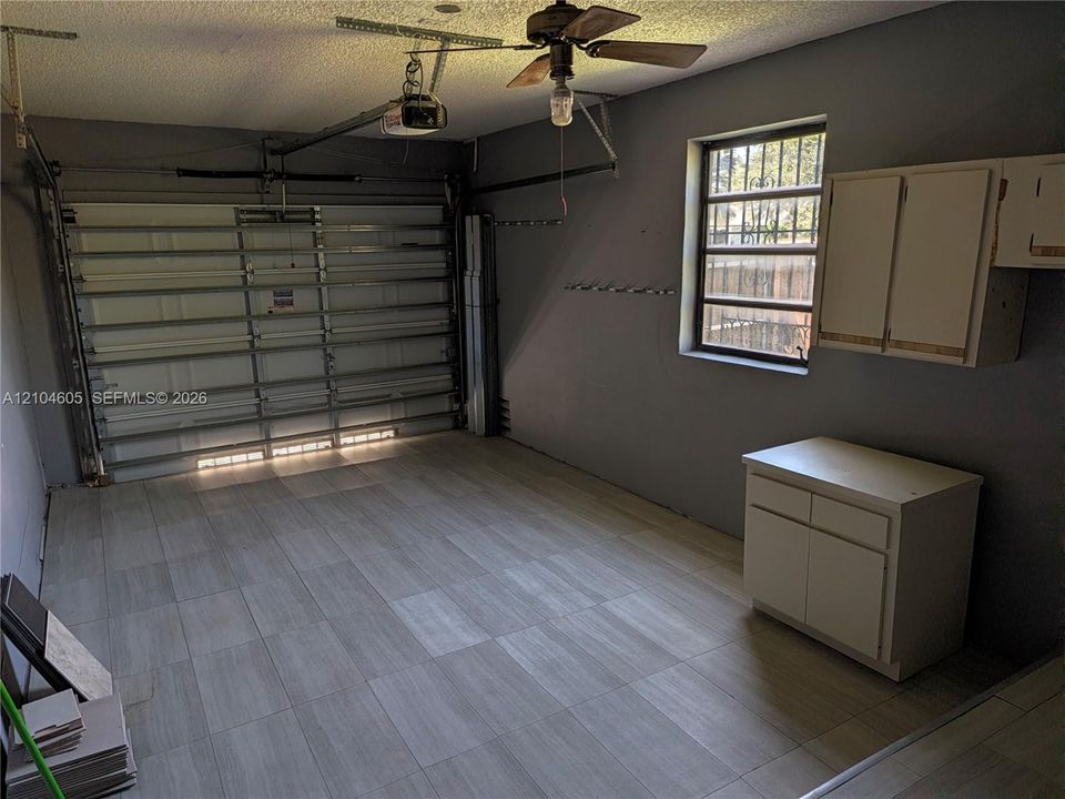 Garage featuring tile flooring, metal sectional garage door, built-in wall and base cabinetry, and ceiling-mounted paddle fan