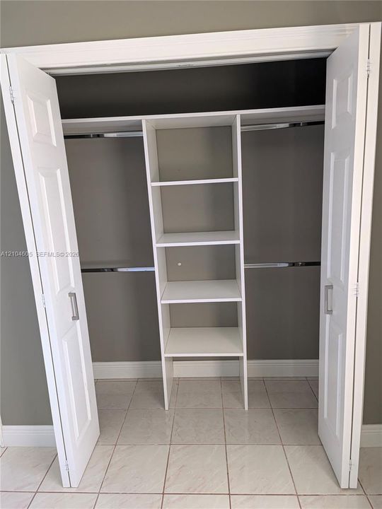 Reach-in closet featuring white bi-fold doors, chrome hanging rods, and integrated floor-to-ceiling shelving