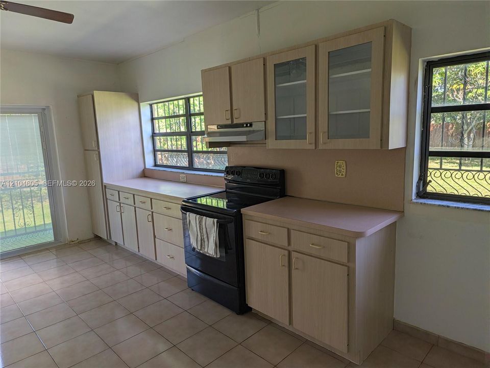 Kitchen featuring light wood-finish cabinetry, glass-front upper cabinet doors, tile flooring, and windows with security bars