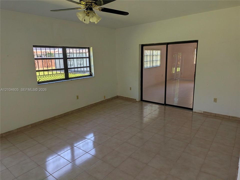 Neutral ceramic tile flooring, sliding glass doors, window with decorative security bars, and a ceiling fan with integrated light fixture