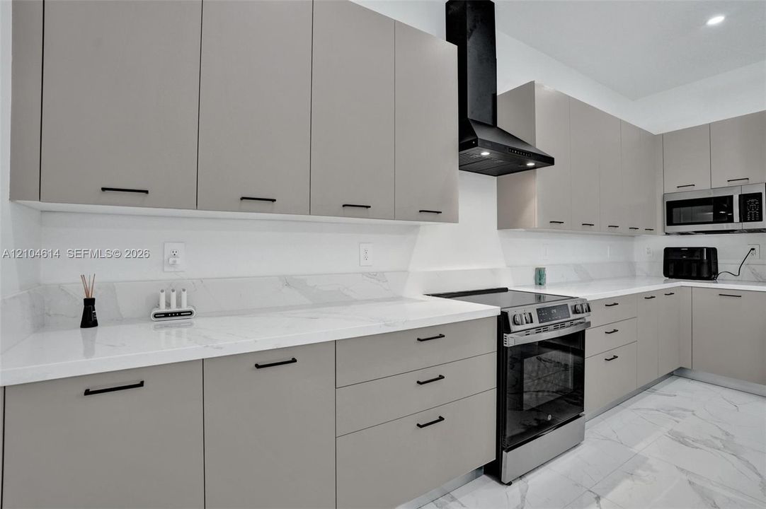 Contemporary kitchen featuring light gray cabinetry, white countertops, stainless steel appliances, and a black range hood