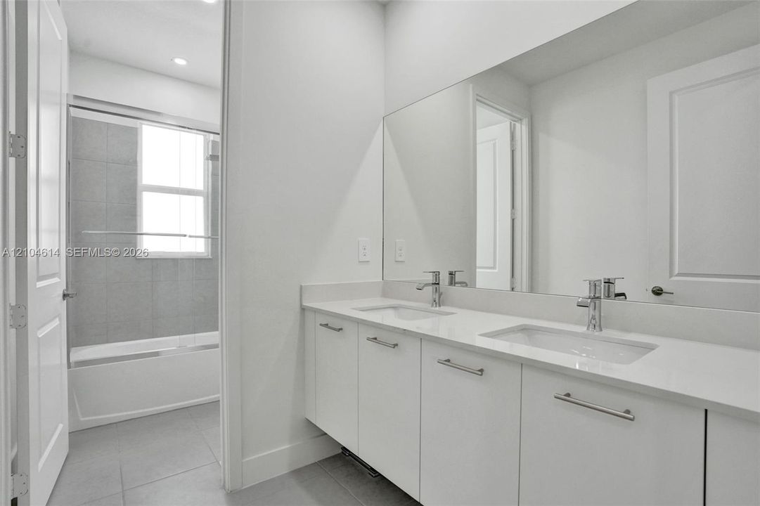 Dual vanity with chrome fixtures and ample counter space, full-width mirror, recessed lighting, and a bathtub with a sliding glass enclosure