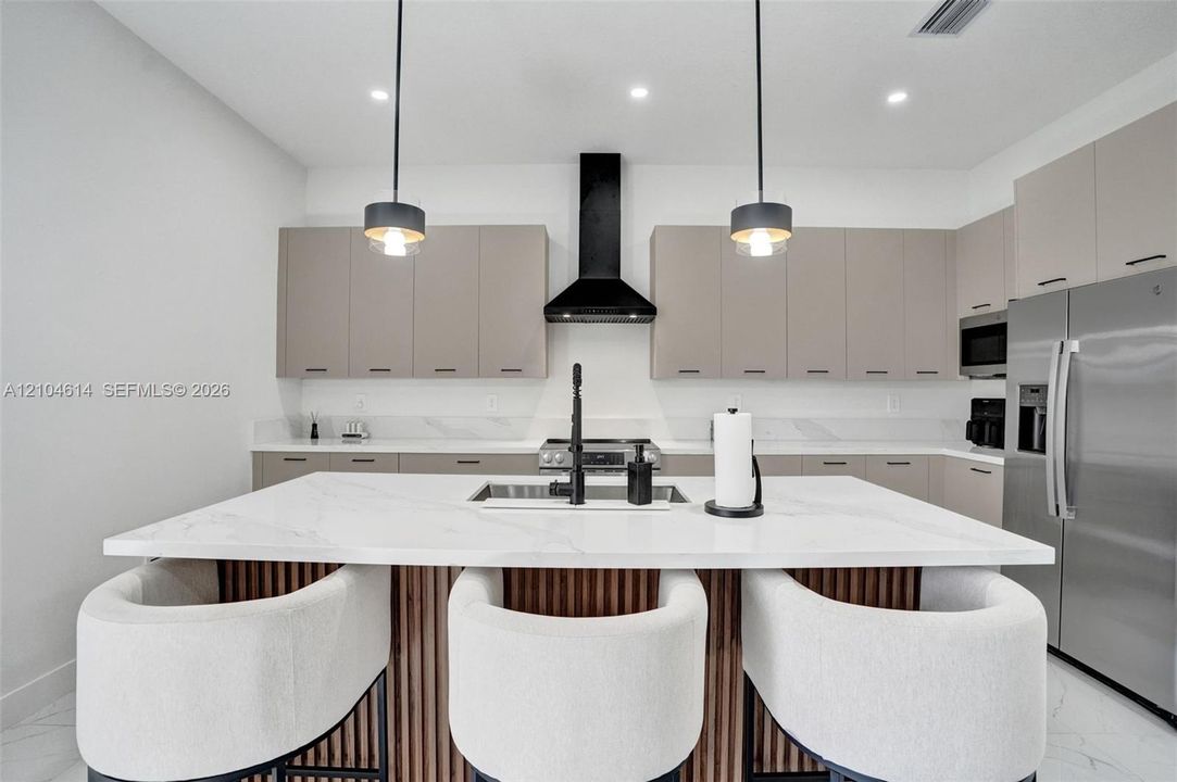 Kitchen featuring a large island with white countertop, integrated sink, and wood-slat detailing