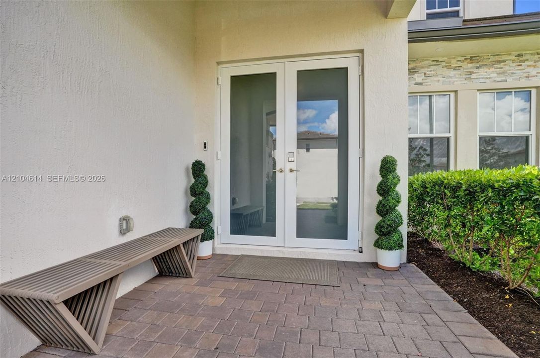 Double glass-paneled entry doors, brick paver patio, stucco exterior, and manicured landscaping