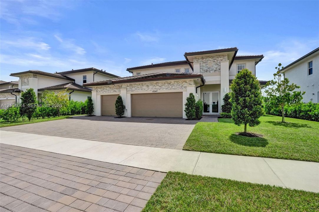 Contemporary stucco exterior with stone accents, featuring a two-car garage, a paver driveway, and a manicured lawn