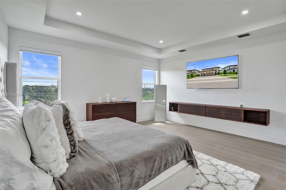 Tray ceiling with recessed lighting, light wood-look flooring, and a built-in floating media cabinet