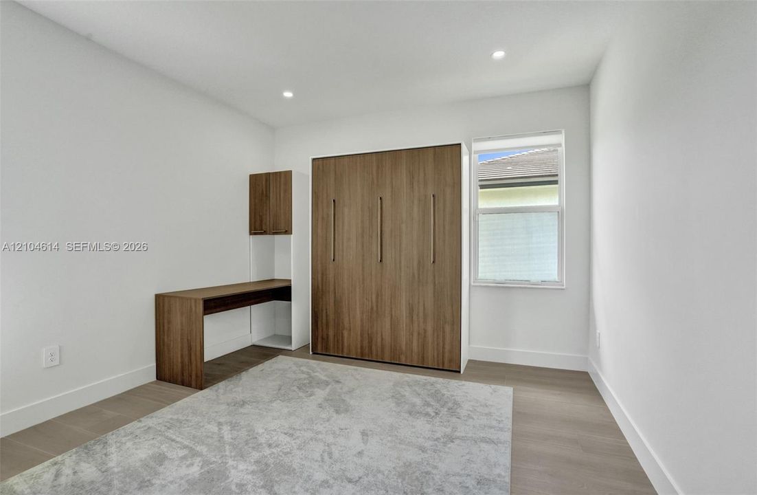 Recessed ceiling lighting, wood look flooring, built-in desk with overhead cabinetry
