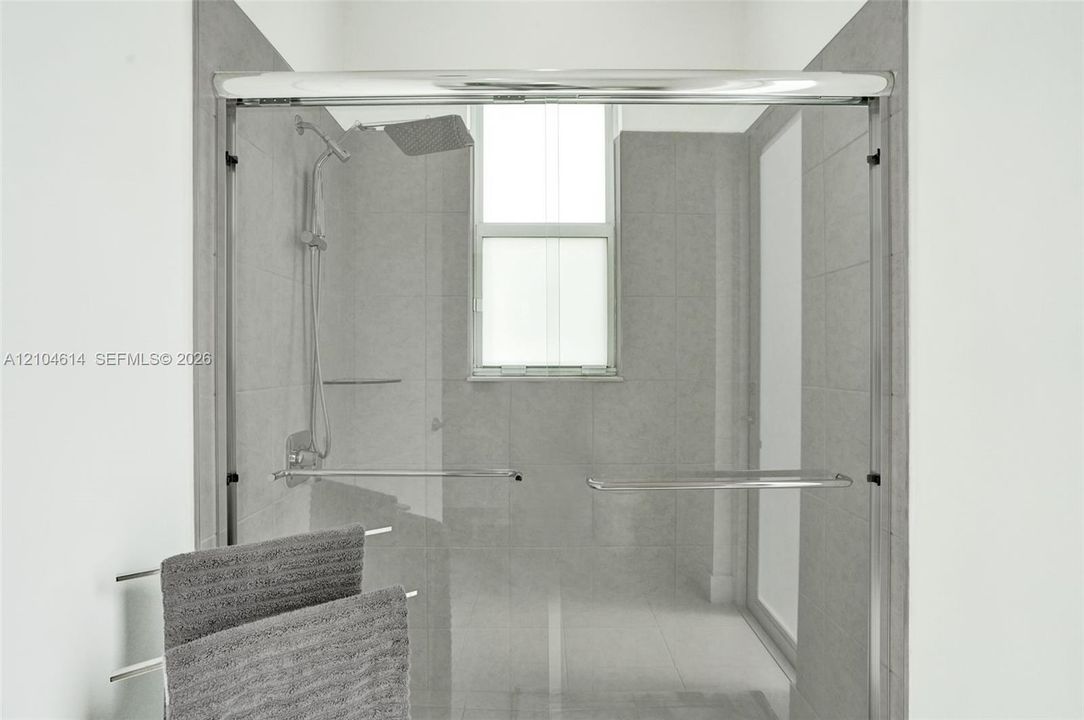 Frameless glass shower enclosure featuring a rainfall showerhead and integrated window