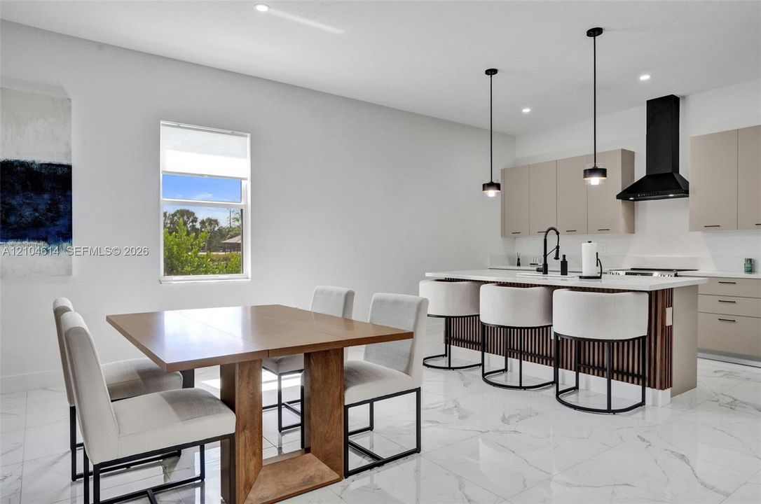 Open-concept living space featuring a modern kitchen with an island, sleek pendant lighting, a contemporary range hood, and light-toned cabinetry