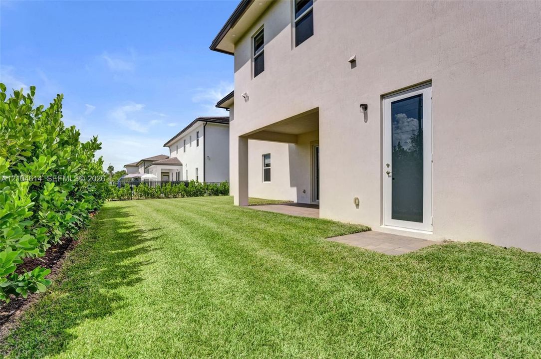 Expansive green lawn with established hedges, featuring a covered patio and a separate exterior door with a full-light panel
