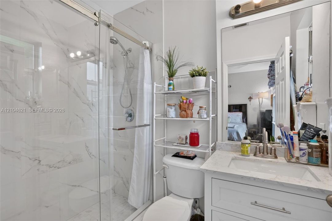 Bathroom featuring a walk-in shower with floor-to-ceiling stone-finish tile, glass enclosure, chrome fixtures, vanity with stone-finish countertop, and wall-mounted mirror