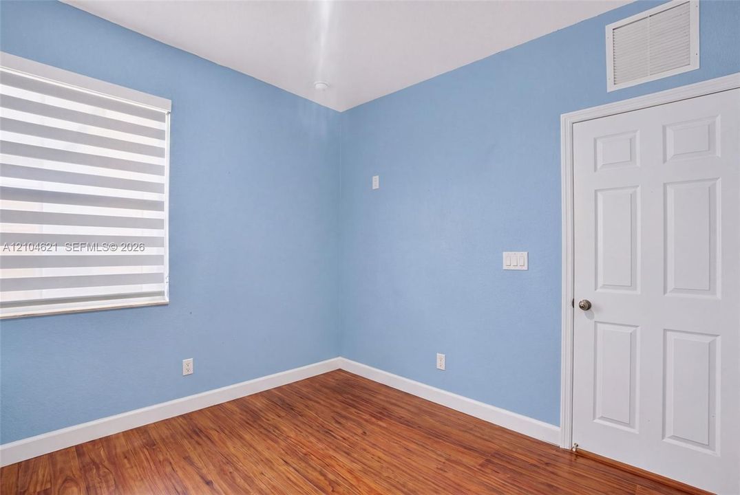 Room featuring wood-finish flooring, blue-toned walls, and a white six-panel door with a metallic knob