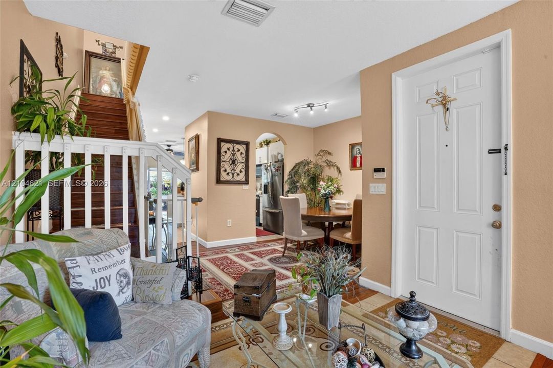 Entryway featuring a white paneled front door, wood-finish staircase with a white balustrade, and a decorative arched passage