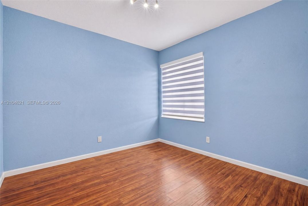 Interior room featuring wood-finish flooring, light blue textured walls, and horizontal zebra-style window shades